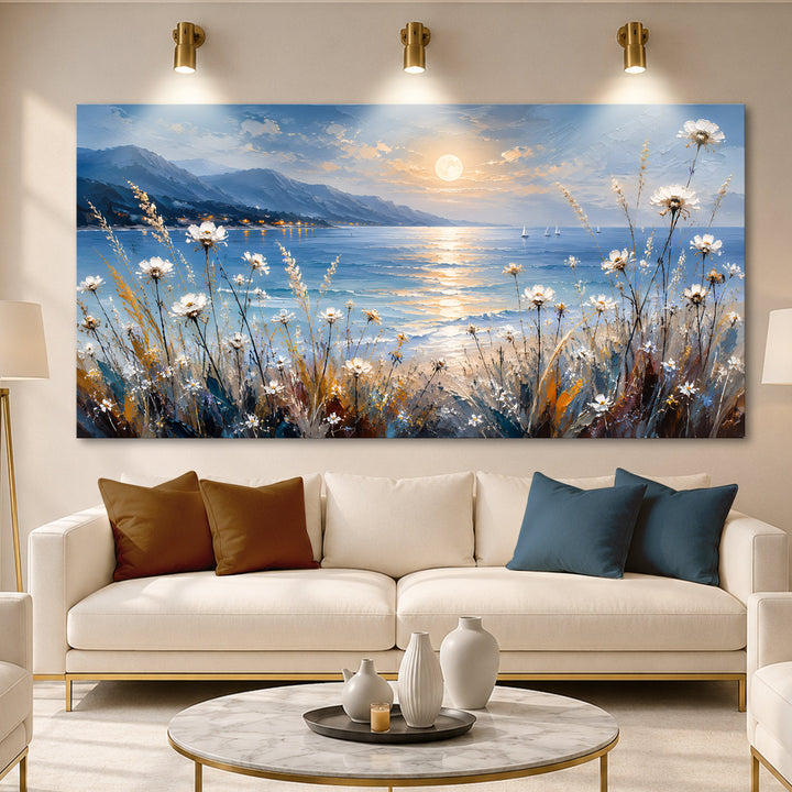 Quadro Luar à Beira-mar acima de sofá creme com almofadas caramelo e azuis, sob arandelas douradas